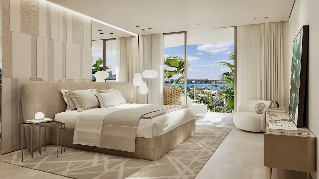 Dormitorio principal con pared de cabecero tapizado, puertas corredizas abiertas a una terraza y la bahía con palmeras al fondo.