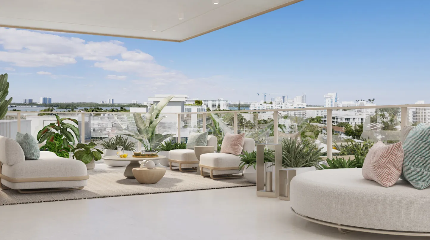Una terraza de Origin amueblada con sillones de fibra tejida, una mesa baja redonda y jardineras, con vista sobre techos de baja altura hacia la bahía.